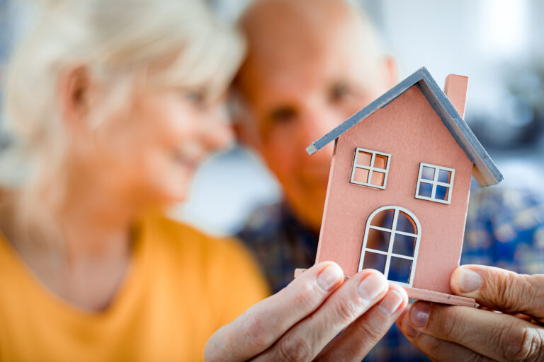 happy senior couple holding small home model